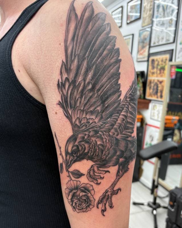 Black and grey realistic bird and rose tattoo on upper arm