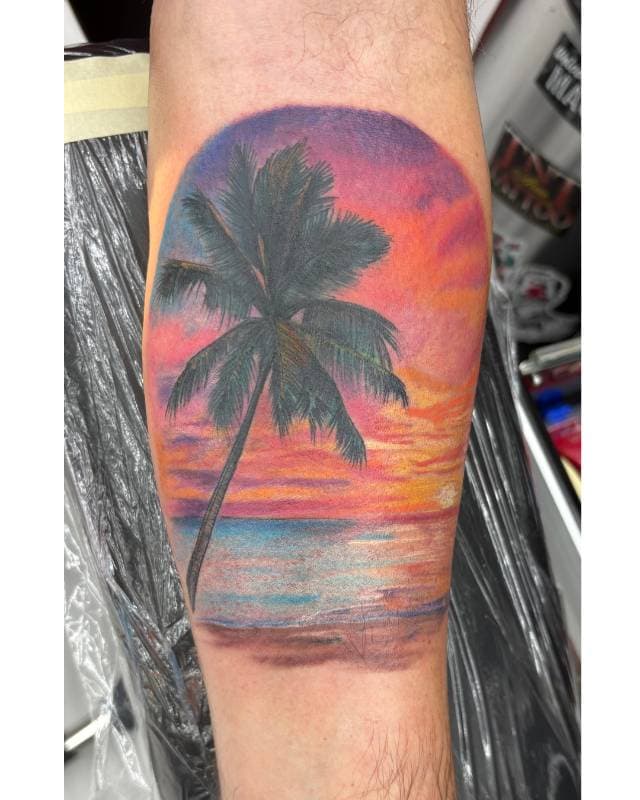 Colorful beach scene forearm tattoo with palm tree and sunset.